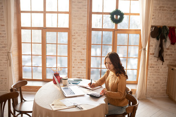 Dark-haired young woman in sweater dealing with calculations