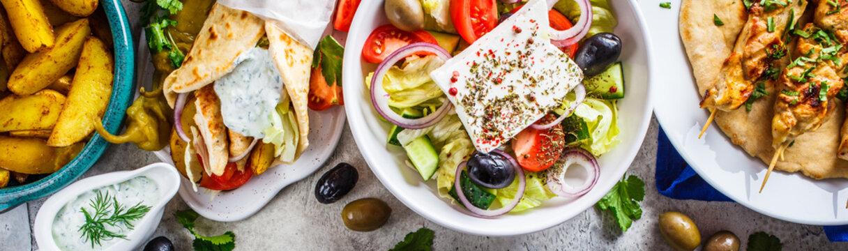 greek food: greek salad, chicken souvlaki, gyros and baked potato wedges on gray background, top vie