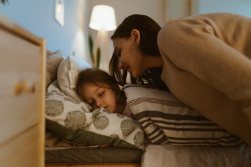 the girl sleeps in bed, mom came to wake her up and gently leaned over her