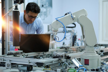 Industry 4.0 workshop in an automation education center. Engineer is programming PLC. Focus on Gripper which picks up the product from an automated car and programming engineer at the background.