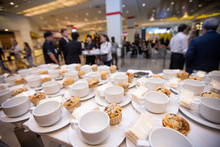 Group Of Empty Coffee Cups With Snack Cake On Plate. Many Rows Of White Cup For Service Hot Tea Or Coffee In Buffet And Seminar Event Over Blurred People Crowd Backgrounds, Shallow Dof Or More Blur
