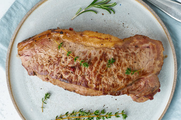 Wall Mural - Keto ketogenic diet beef steak, striploin on gray plate on white background. Paleo food recipe with whole big piece of meat and seasoning. Macro, close up, top view