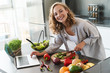 Happy young woman making a salad at the kitchen