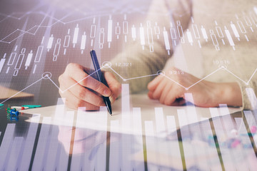 Hand taking notes in notepad. Forex chart holograms in front. Concept of research. Multi exposure