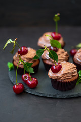 Wall Mural - Chocolate cupcakes with ripe red cherries and cheese cream on dark wooden background. Selective focus. Unhealthy food