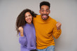 © timtimphoto - Portrait of cheerful young pretty dark skinned brunette pair looking happily at camera and raising fists joyfully, rejoicing together about nice occasion, isolated over grey background