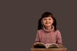 © Marharyta Hanhalo - Cute and happy baby girl sitting at a desk with a book and preparing to go to elementary school, reading a book and improving her fast reading skills
