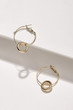 Subject shot of a pair of hoop earrings isolated on the white geometric design surface. Each metal earring is made as a golden ring with a pendant in the form of a thick silver ring.