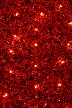 Red Christmas Festive Decorative Background With Tinsel, Flashing Lights And Garlands. New Year Lighting Decoration In Red And Yellow Color. Wall Illuminated By Christmas String Rice Lights Bulbs.