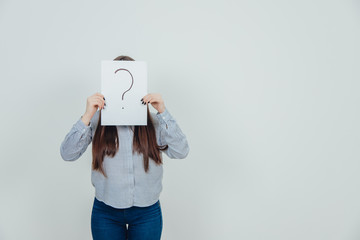 Inquisitive asian student girl hiding her face behind a sheet of paper with question mark written on it.