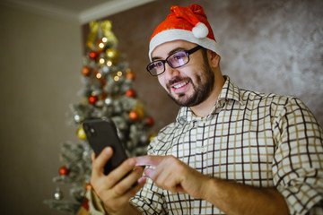 Portrait of a man holding the phone in his hand near the Christmas tree.