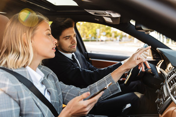 Wall Mural - Photo of man and woman talking and using cellphone while driving in car