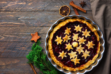 Home baked puff pastry Christmas New years pie torte with plum cinnamon jam filling decorated with stars in rustic baking form on wood table. Holiday baking concept