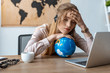 © LIGHTFIELD STUDIOS - tired travel agent leaning on globe while sitting at workplace with closed eyes