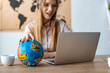 © LIGHTFIELD STUDIOS - selective focus of smiling travel agent touching globe while looking at laptop