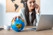 © LIGHTFIELD STUDIOS - selective focus of travel agent holding hand on globe while working at workplace
