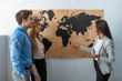 © LIGHTFIELD STUDIOS - smiling travel agent pointing with finger at map on wall near couple of tourists