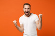 © ViDi Studio - Overjoyed young man in casual white t-shirt posing isolated on orange background, studio portrait. People sincere emotions lifestyle concept. Mock up copy space. Clenching fists like winner screaming.