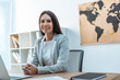 © LIGHTFIELD STUDIOS - attractive travel agent looking at camera while sitting at workplace