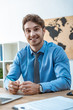 © LIGHTFIELD STUDIOS - handsome travel agent smiling at camera while sitting at workplace