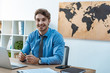 © LIGHTFIELD STUDIOS - handsome travel agent smiling at camera while sitting at workplace