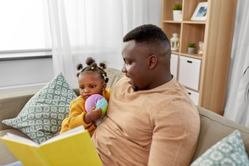 family, fatherhood and people concept - happy african american father reading book for baby daughter at home