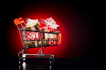 Shopping cart trolley full of colorful gift boxes on red background