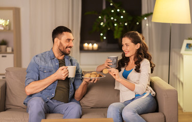 Poster - leisure and people concept - happy couple drinking tea or coffee with cookies at home