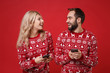 © ViDi Studio - Laughing young couple guy girl in Christmas knitted sweaters posing isolated on red background. New Year 2020 celebration holiday concept. Mock up copy space. Using mobile phone typing sms message.