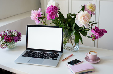Female office desk workspace homeoffice mock up with laptop, pink peony flowers bouquet, smartphone, pink accessories and pink cup of coffee. Fashion, beauty or lifestyle blog concept.
