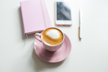 Pink notebook and cup of cappuccino coffee with pink tulips on white background. Pink writing set with cappuccino. Woman's workplace in pink. Flat lay. Top view. Copy space