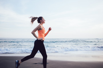 Young athletic sportswoman jogging on sea beach