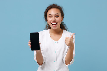 Wall Mural - African american doctor woman isolated on blue background. Doctor in medical gown hold mobile phone with blank empty screen showing thumb up. Healthcare personnel medicine concept. Mock up copy space.