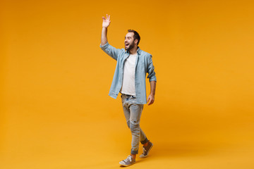 Poster - Cheerful young bearded man in casual blue shirt posing isolated on yellow orange background in studio. People lifestyle concept. Mock up copy space. Waving and greeting with hand as notices someone.