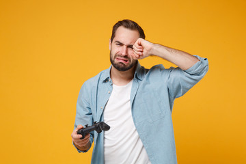 Wall Mural - Displeased young man in casual blue shirt posing isolated on yellow orange background, studio portrait. People sincere emotions lifestyle concept. Mock up copy space. Hold joystick play game crying.