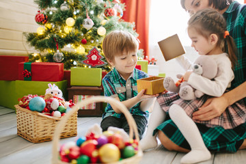 Wall Mural - Happy family mom, son and daughter on a Christmas winter sunny morning in a decorated Christmas celebration room with a Xmas tree and gifts.