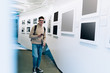 © GalakticDreamer - Smiling young man standing near wall with frames at exhibition