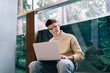 © GalakticDreamer - Smiling young man in glasses with laptop on knees looking at camera near aquarium
