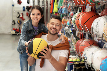 Poster - Little school girl with father choosing ball in supermarket