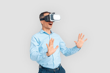 Wall Mural - Freestyle. Mature businessman in virtual reality headset standing isolated on white playing touching space excited