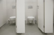 Toilet bowls in public bathroom, restroom or WC maintained in sterile condition for high standards of lavatory hygiene. Interior photo in shades of white of gray. 