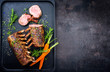 Barbecue rack of lamb with carrot and herbs offered as top view on a modern design cast iron tray with copy space right