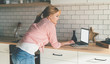 © GalakticDreamer - Young woman watching video on laptop standing in kitchen cooking
