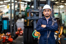 Portrait Of Asian Mechanic Fold Over Holding A Wrench And Smiling At Truck And Forklift Garage. Industrial Mechanic Engineer In Hard Hat