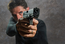 Shallow Depth Of Focus Action Portrait Of Serious And Attractive Hitman Or Special Agent Man Holding Gun Pointing The Weapon Isolated On Dark Background