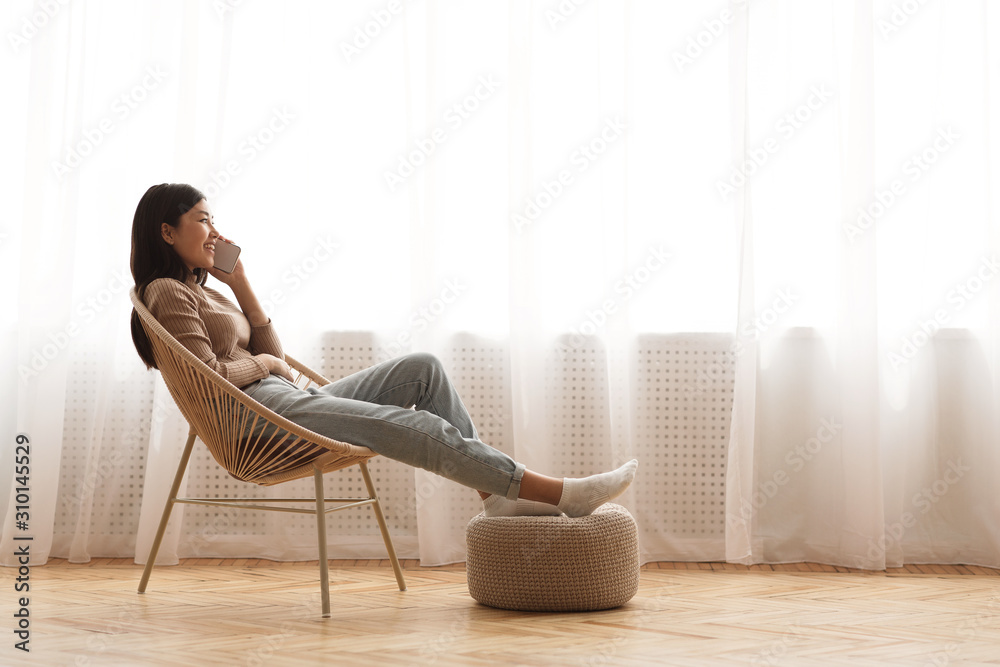 Teen girl relaxing in modern armchair and talking on phone - obrazy, fototapety, plakaty 