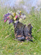 Old Hiking Shoes With A Bouquet Of Wild Flowers On The Grass In A Meadow