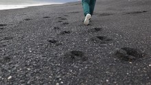 Woman walking on the black sand beach leaving footprints