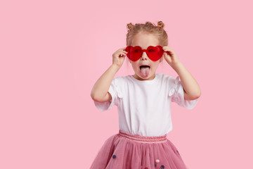 Portrait of surprised cute little toddler girl in the heart shape sunglasses. Child with open mouth having fun isolated over pink background. Looking at camera. Wow funny face.