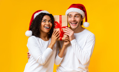 Wall Mural - portrait of happy couple holding gift box and wearing santa hats